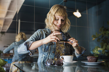 Frau fotografiert Kaffeetasse auf Tisch durch Smartphone in Café - CAVF19072