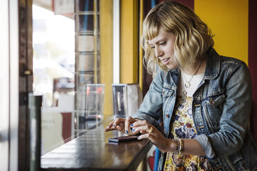 Woman using smart phone by window in cafe - CAVF19077