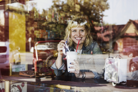 Glückliche Frau schaut weg, während sie ein Glas Milchshake in einem Café hält, lizenzfreies Stockfoto