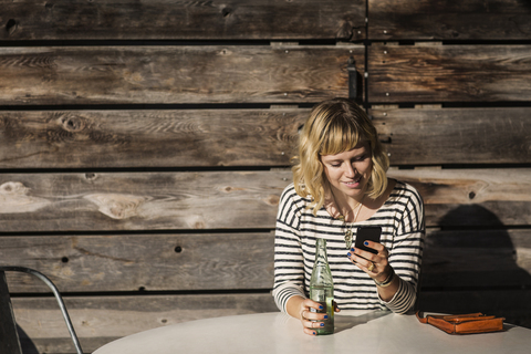 Frau, die in einem Café sitzt und ihr Smartphone benutzt, lizenzfreies Stockfoto