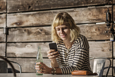 Frau, die ein Smartphone benutzt, während sie eine Limonadenflasche in einem Cafe hält - CAVF19085