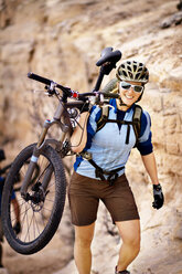 Porträt einer Frau, die ein Fahrrad trägt und auf einem Berg spazieren geht - CAVF19207