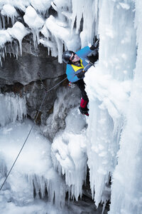 Hochformatige Ansicht eines Mannes mit Eispickel beim Klettern auf einem Eisberg - CAVF19215