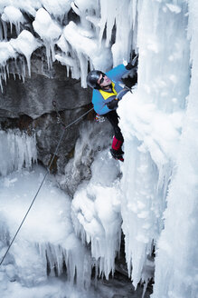 Hochformatige Ansicht eines Mannes mit Eispickel beim Klettern auf einem Eisberg - CAVF19215