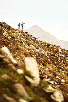 Distant view of hiker pointing at something to friend while standing on mountain with dog - CAVF19334