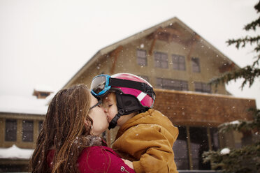 Mutter küsst ihren Sohn bei Schneefall vor dem Ferienort - CAVF19382