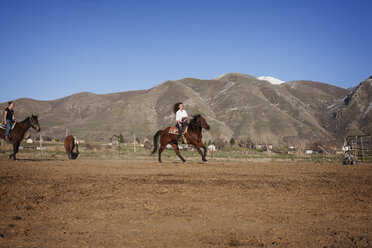 Weibliche Teenager reiten auf einem Pferd in einem Feld gegen den klaren Himmel - CAVF19427