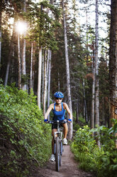 Female athlete cycling on field in forest - CAVF19432