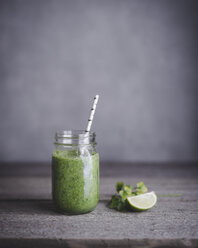 Green smoothie in mason jar with lime on table - CAVF19474