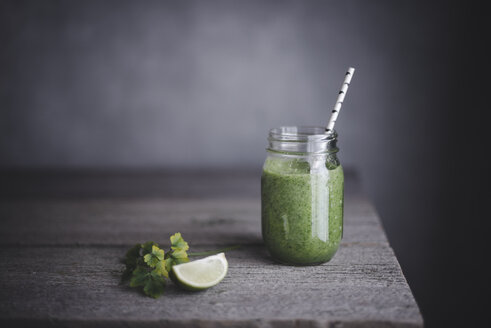 Gesunder grüner Smoothie im Einmachglas mit Limette auf dem Tisch - CAVF19475