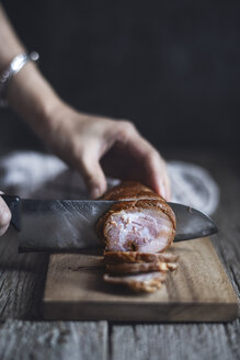 Ausgeschnittenes Bild einer Frau, die zu Hause Schweinefleisch auf einem Schneidebrett schneidet - CAVF19509