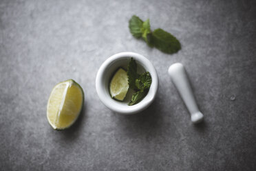 Overhead view of lemon and mint leaves in mortar by pestle on kitchen counter - CAVF19527