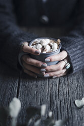 Cropped image of woman holding mug of hot chocolate topped with marshmallows at wooden table - CAVF19631