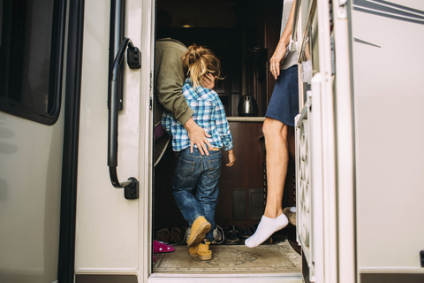 Mutter, die ihre Tochter umarmt, während sie mit ihrem Mann im Wohnmobil steht, lizenzfreies Stockfoto