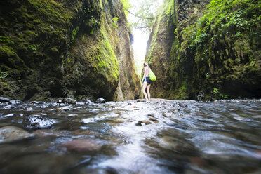 Female hiker standing on river amidst mountains - CAVF19724