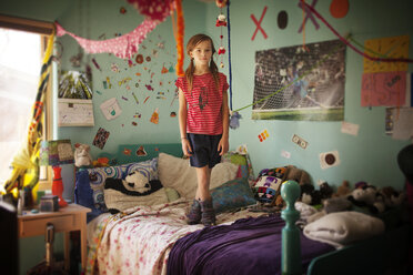 Porträt eines Mädchens, das auf einem Bett im Zimmer steht - CAVF19726