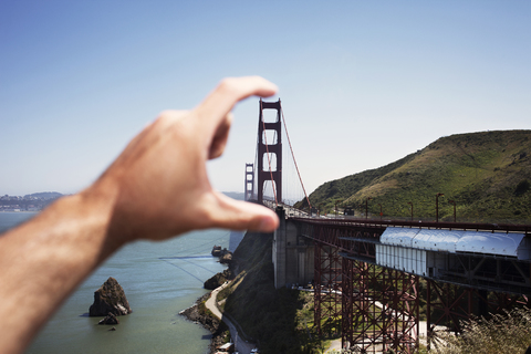 Optische Täuschung einer Männerhand, die die Golden Gate Bridge gegen den klaren Himmel hält, lizenzfreies Stockfoto