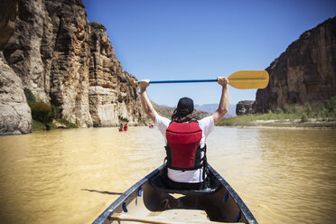 Rückansicht eines Mannes, der ein Ruder hält, während er in einem Boot auf dem Fluss im Big Bend National Park sitzt - CAVF19746