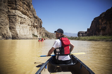 Porträt eines lächelnden Mannes mit Ruder, der in einem Boot auf einem Fluss im Big Bend National Park sitzt - CAVF19748