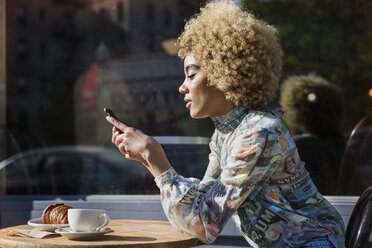 Seitenansicht einer Frau, die am Tisch eines Straßencafés sitzt und SMS schreibt - CAVF19754