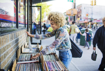 Seitenansicht einer lächelnden Frau, die vor einem Geschäft in der Stadt nach Schallplatten sucht - CAVF19756