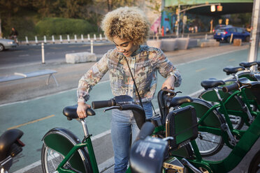 Glückliche Frau, die ein Fahrrad auf einer Straße in der Stadt mietet - CAVF19764