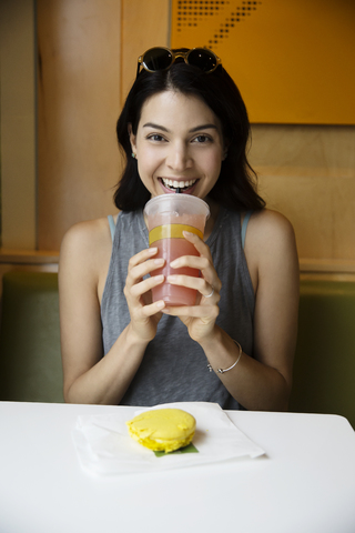 Porträt einer glücklichen Frau, die in einem Restaurant Saft trinkt und Makronen isst, lizenzfreies Stockfoto