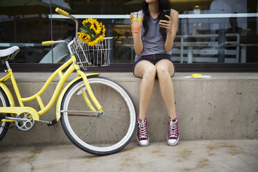 Low section of woman sitting on retaining wall by bicycle - CAVF19787