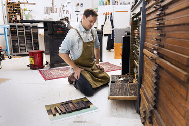 Nachdenklicher Mann betrachtet Holzalphabete in einer Druckerpresse - CAVF19813
