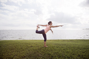 Side view of woman exercising on grassy field against sea - CAVF19857