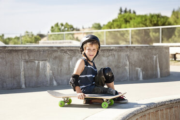 Portrait of happy boy sitting at skateboard park - CAVF19866