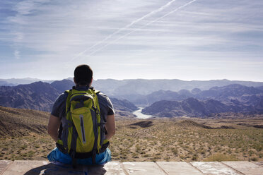 Hiker looking at mountains while sitting on retaining wall - CAVF19889