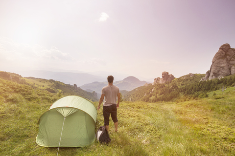 Rückansicht eines Wanderers, der am Zelt auf einem Hügel steht, gegen den Himmel, lizenzfreies Stockfoto