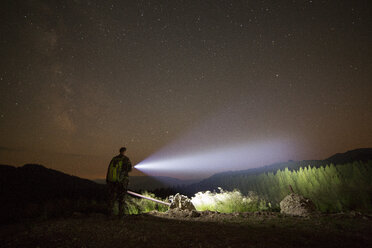 Wanderer mit beleuchteter Taschenlampe steht auf einem Hügel vor dem Sternenhimmel - CAVF19902