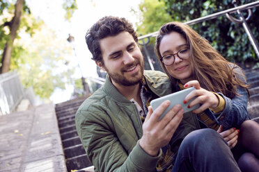 Happy young couple using smart phone while sitting on steps - CAVF19912