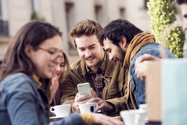 Glückliche Freunde, die in einem Straßencafé gemeinsam ihr Smartphone benutzen - CAVF19921