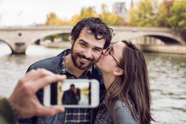 Cropped image of friend photographing couple through smart phone by river - CAVF19935