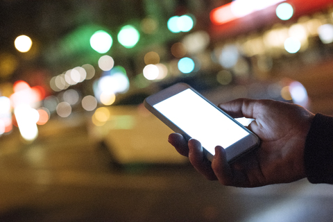 Abgeschnittene Hand hält Smartphone in beleuchteter Stadt bei Nacht, lizenzfreies Stockfoto