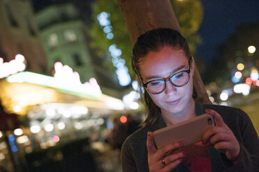 Junge Frau benutzt Smartphone in beleuchteter Stadt bei Nacht - CAVF19940