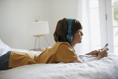 Seitenansicht eines Jungen, der Musik hört, während er zu Hause auf dem Bett liegt - CAVF19972