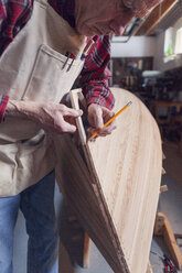 Senior man using pencil on wooden boat in workshop - CAVF20004