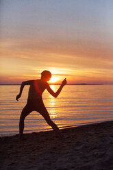 Silhouette of boy throwing stone in water at beach - CAVF20009