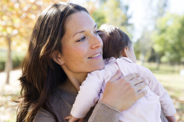 Smiling mother carrying toddler while standing at park - CAVF20026