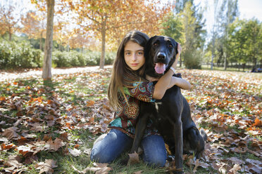 Portrait of girl with black dog sitting at park during autumn - CAVF20031