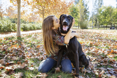 Mädchen küsst schwarzen Hund, während sie im Herbst im Park sitzt - CAVF20032