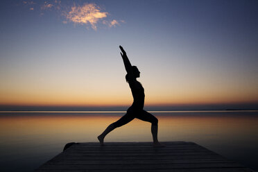 Silhouette woman exercising on pier against sky during sunset - CAVF20036