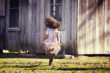 Rückansicht eines Mädchens, das auf einer Wiese gegen ein Haus läuft - CAVF20059