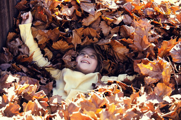 Hoher Blickwinkel eines Mädchens, das auf Herbstblättern auf einem Feld liegt - CAVF20060