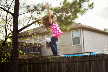 Happy girl with arms raised jumping at backyard - CAVF20068