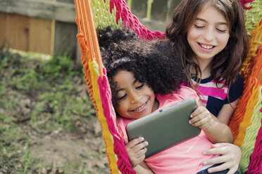 Happy siblings using tablet while sitting on hammock at backyard - CAVF20070